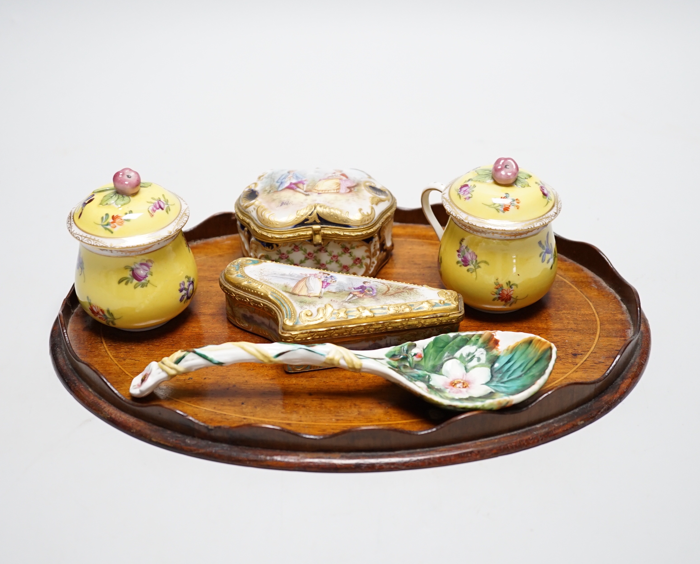 A small oval mahogany tray and German decorative porcelain cups and covers, two trinket boxes and a spoon
